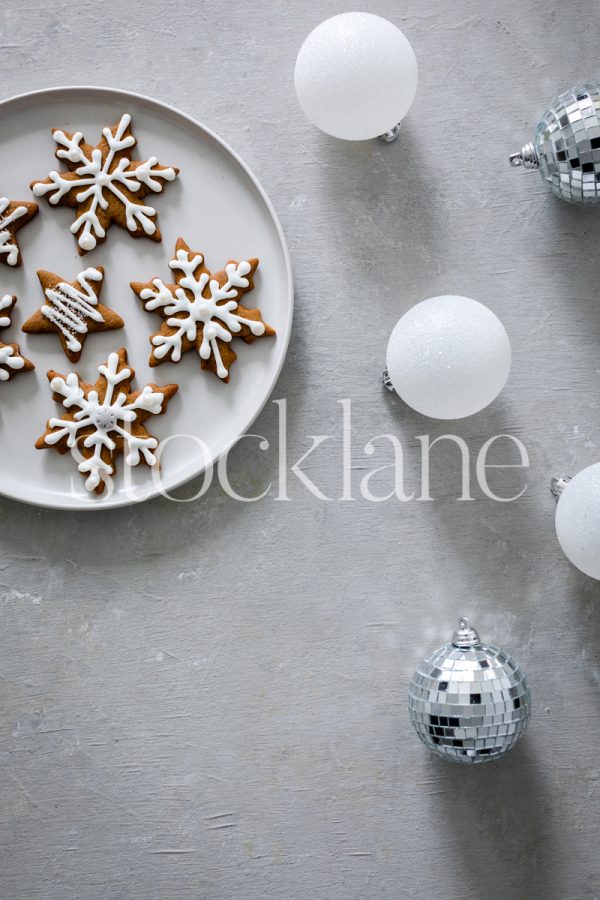 Vertical stock photo of a plate of gingerbread cookies with white and silver Christmas ornaments.