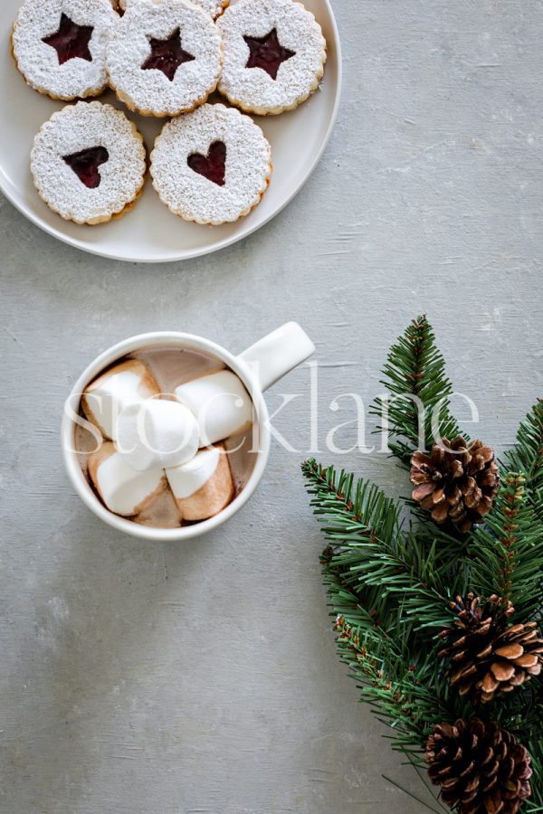 Vertical stock photo of a cup of hot cocoa, a plate of linzer cookies and Christmas greenery.