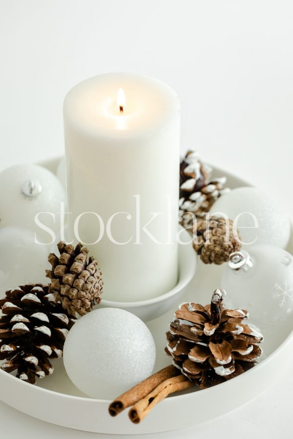 Vertical stock photo of white Christmas ornaments with pinecones and a candle.