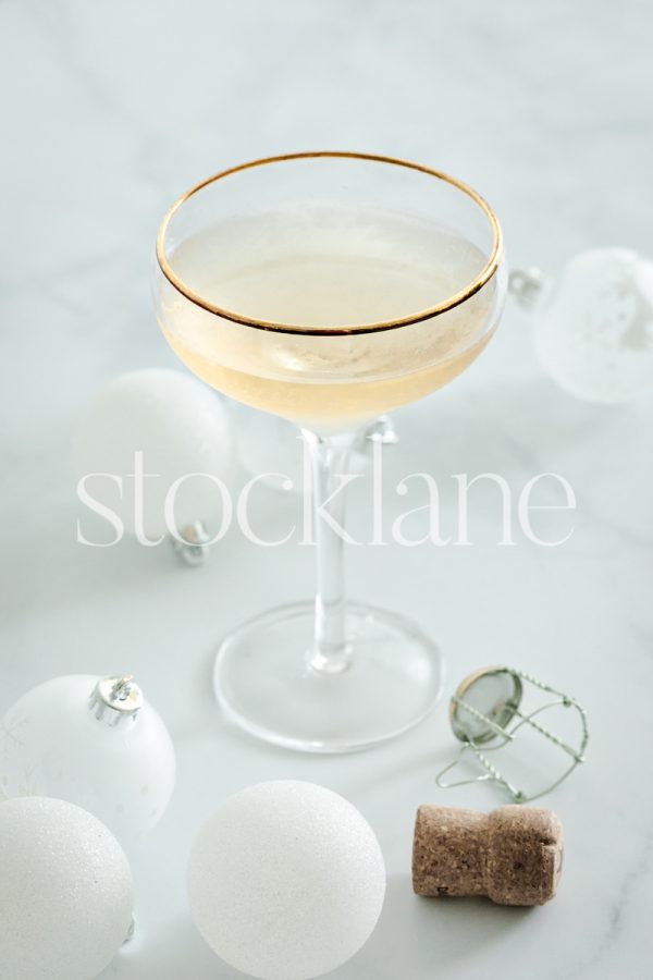 Vertical stock photo of a glass of champagne and white Christmas ornaments.