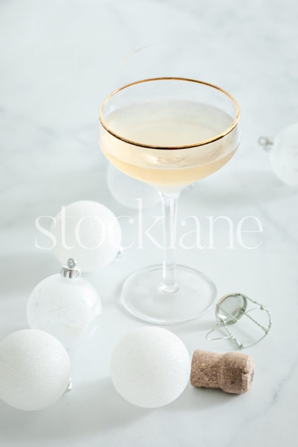 Vertical stock photo of a glass of champagne and white Christmas ornaments.