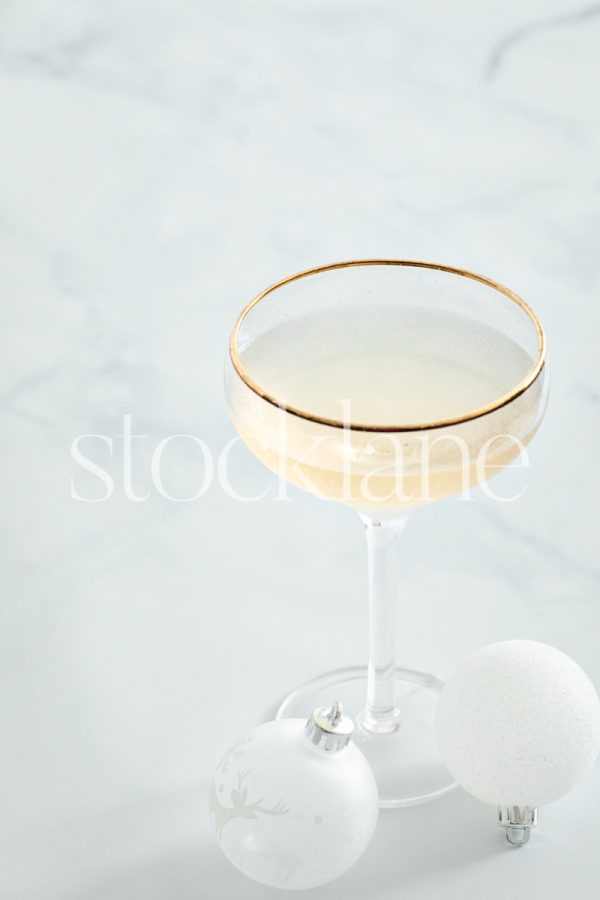 Vertical stock photo of a glass of champagne and white Christmas ornaments.