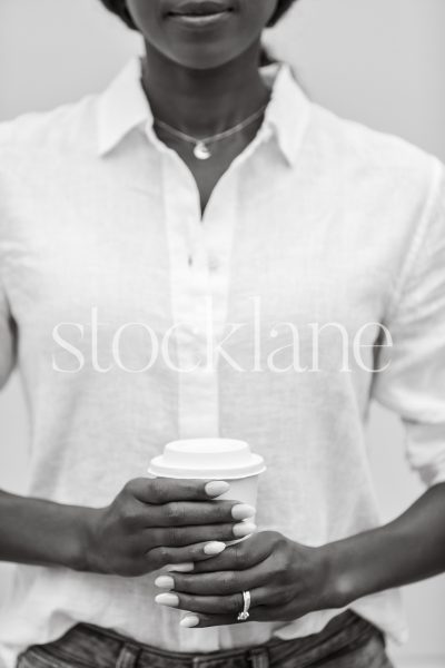 Vertical black and white stock photo of a woman holding a cup of coffee.