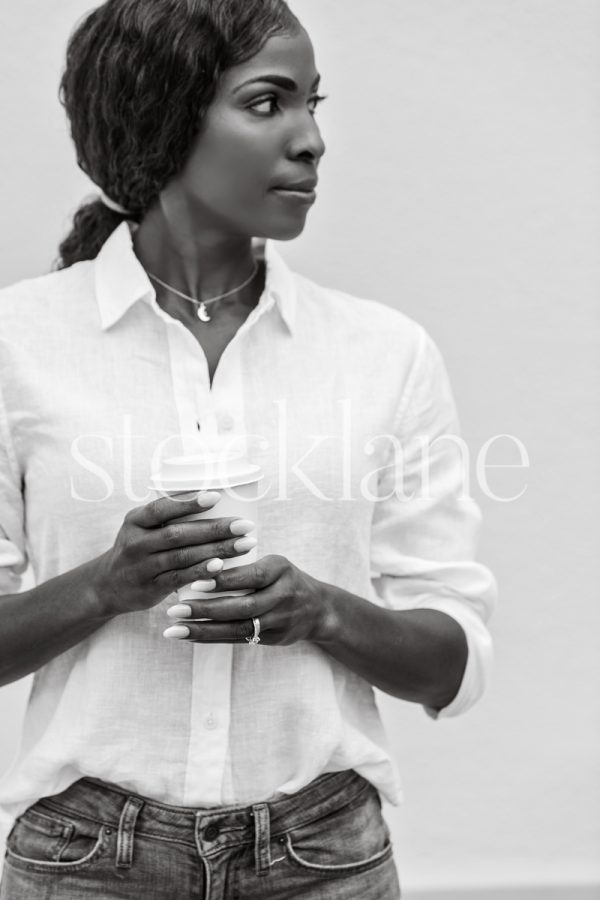 Vertical black and white stock photo of a woman holding a disposable cup of coffee.