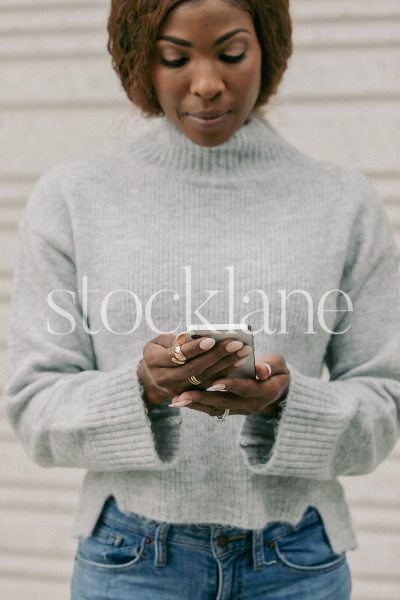 Vertical stock photo of a woman wearing a light gray sweater, holding a phone.