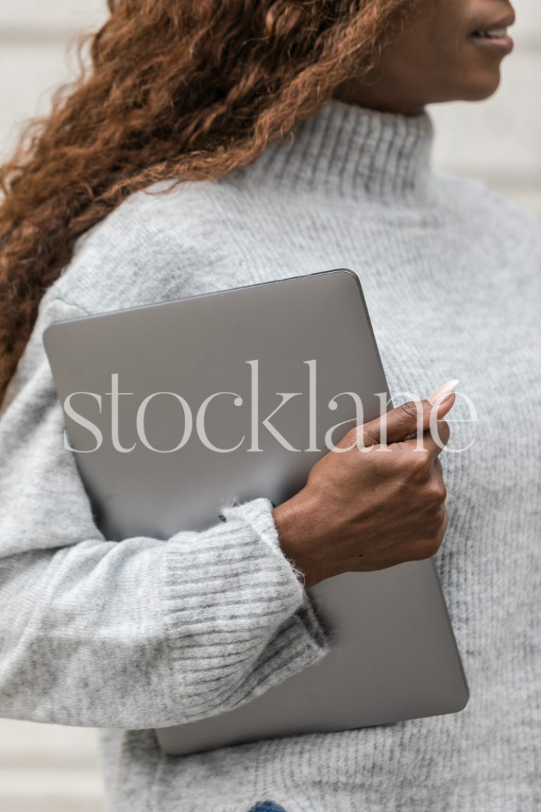 Vertical stock photo of a woman wearing a gray sweater holding a laptop computer.