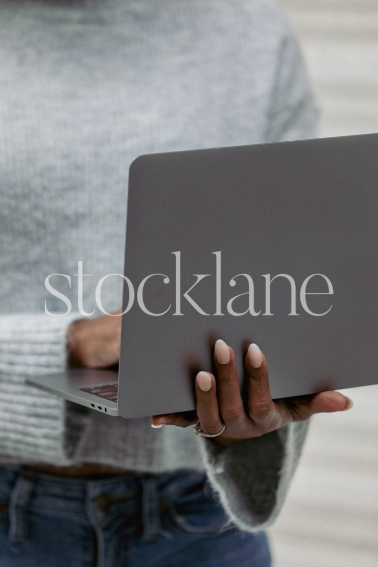 Vertical stock photo of a woman wearing a gray sweater holding a laptop computer.