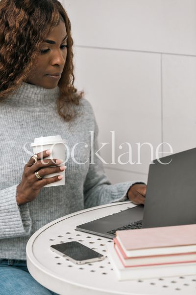 Vertical stock photo of a woman having a cup of coffee while working on her laptop computer.