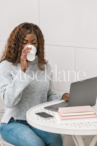 Vertical stock photo of a woman having a cup of coffee while working on her laptop computer.