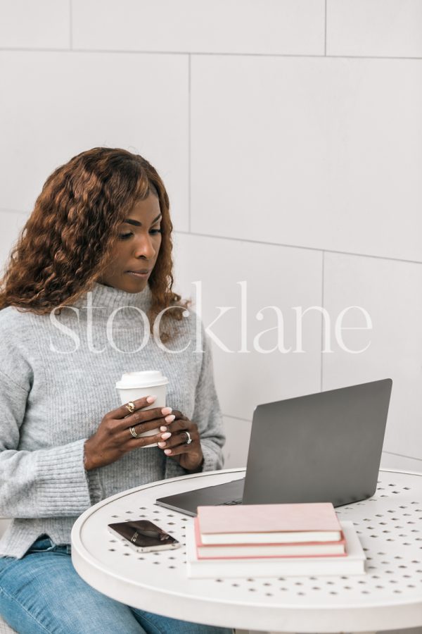 Vertical stock photo of a woman having a cup of coffee while working on her laptop computer.