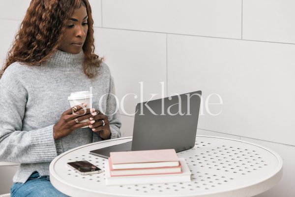 Horizontal stock photo of a woman having a cup of coffee while working on her laptop computer.