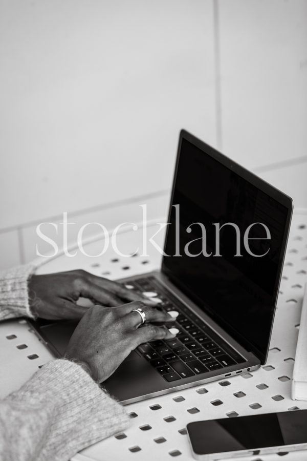 Vertical black and white stock photo of a woman's hands over the keyboard of a laptop computer.