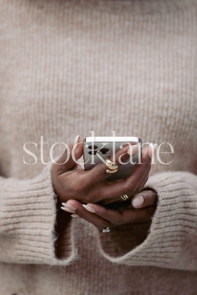 Vertical stock photo of a woman wearing a neutral colored sweater, holding a phone.