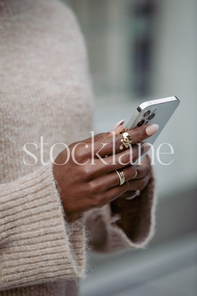 Vertical stock photo of a woman wearing a neutral colored sweater, holding a phone.