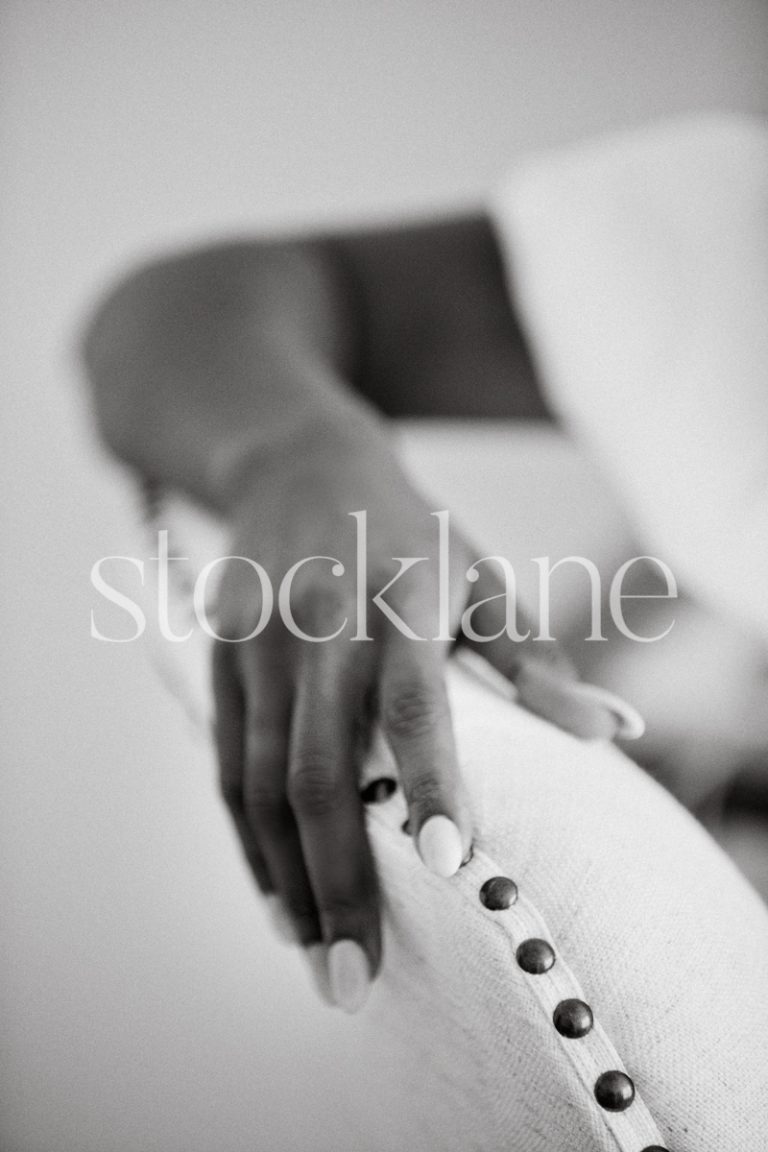 Vertical black and white photo of a woman's arm resting on a chair.