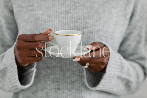 Horizontal stock photo of a woman wearing a light gray sweater, holding a cup.