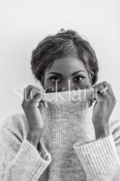 Vertical black and white stock photo of a woman pulling up her sweater over her face.