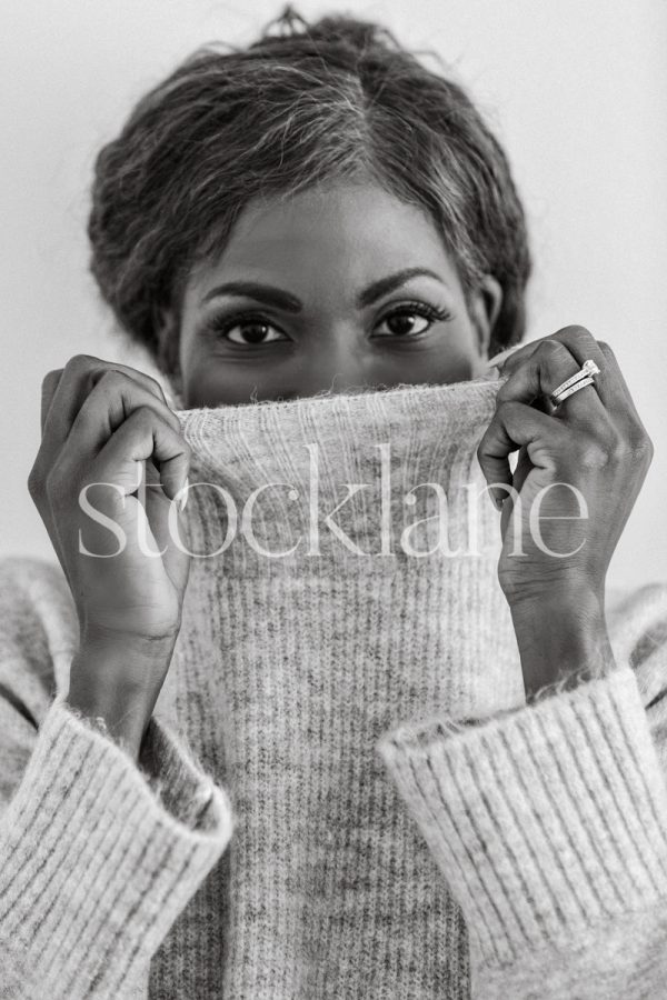 Vertical black and white stock photo of a woman pulling up her sweater over her face.