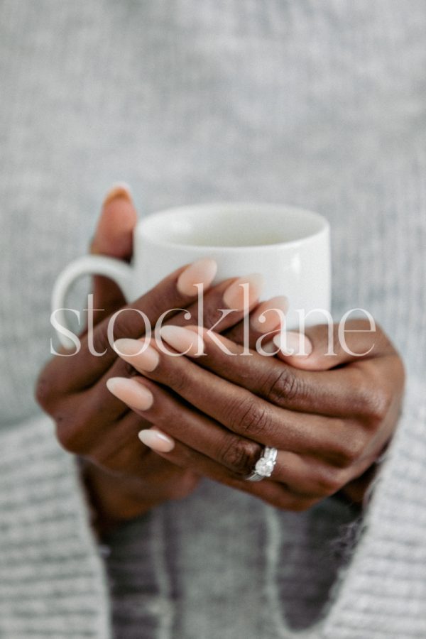 Vertical stock photo of a woman wearing a gray sweater holding a cup.