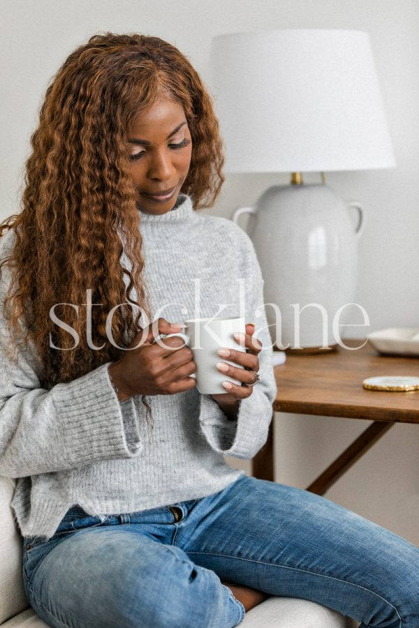 Vertical stock photo of a woman sitting at her desk, having a cup of coffee.