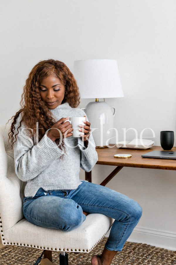 Vertical stock photo of a woman sitting at her desk, having a cup of coffee.