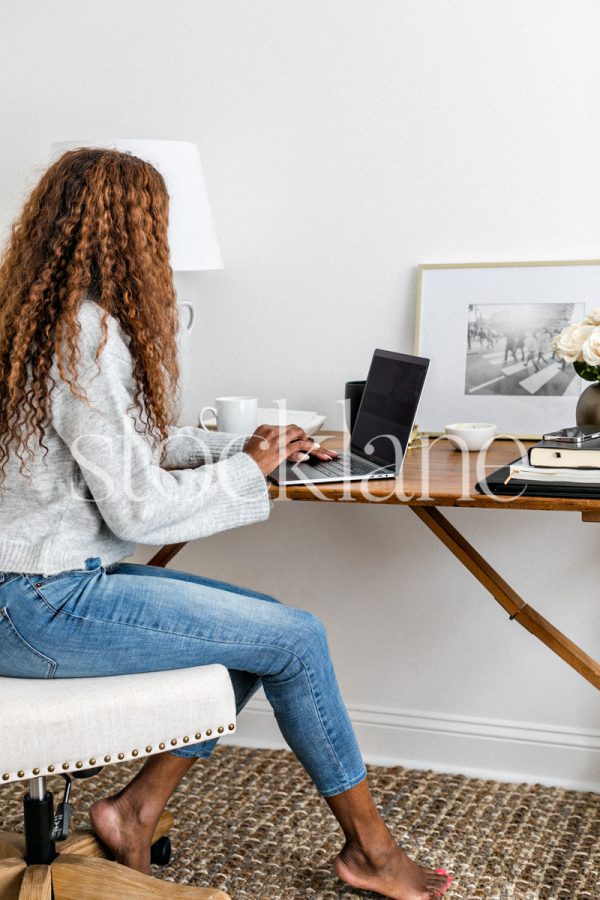 Vertical stock photo of a woman casually dressed, working at her desk.