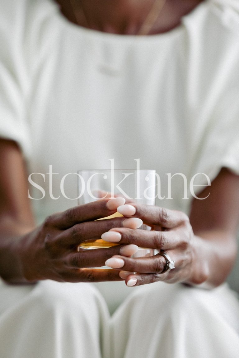 Vertical stock photo of a woman dressed in a white jumpsuit holding a drink.