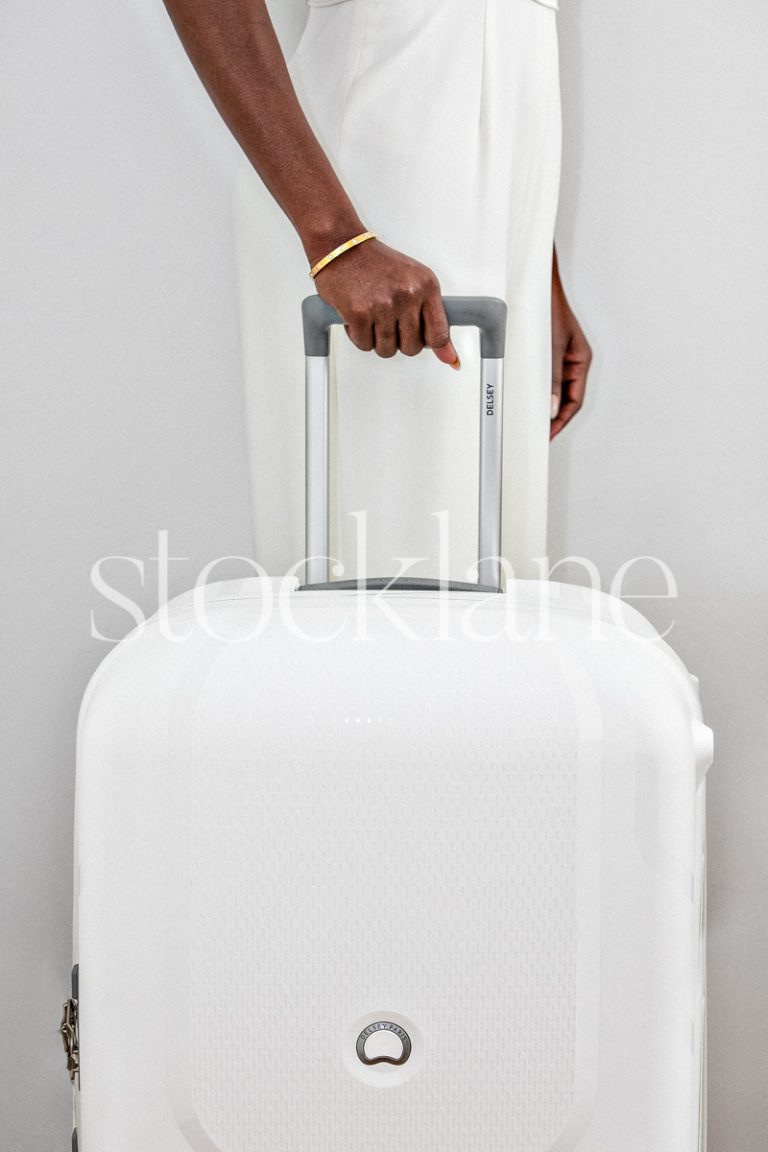 Vertical stock photo of a woman dressed in white holding a white suitcase.