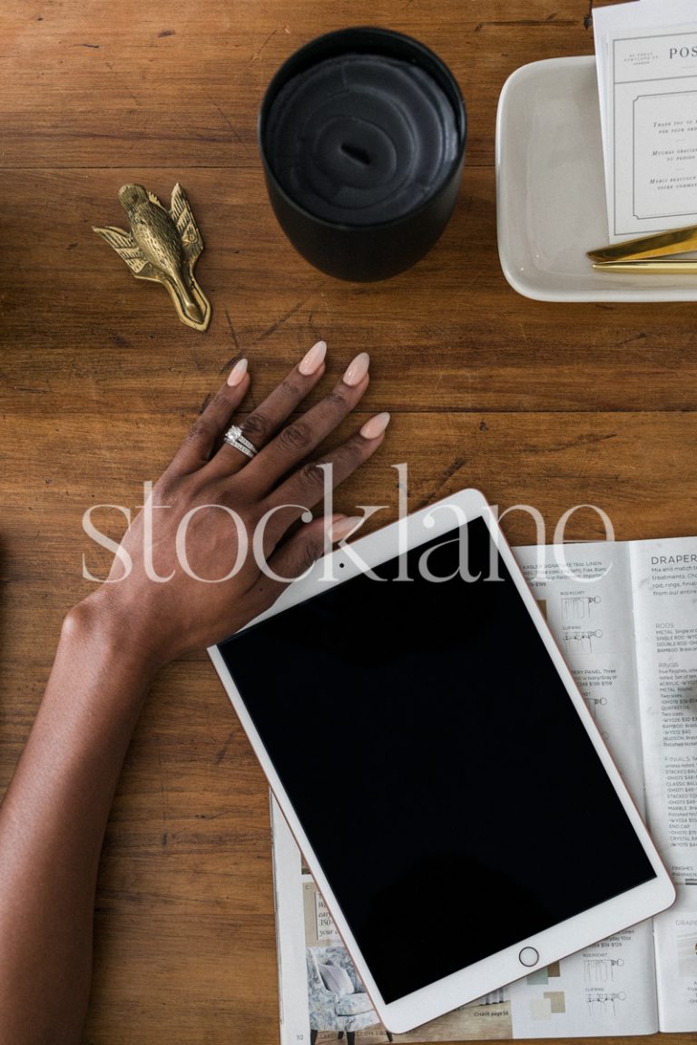 Vertical stock photo of a woman's hand next to her iPad, on a desk.