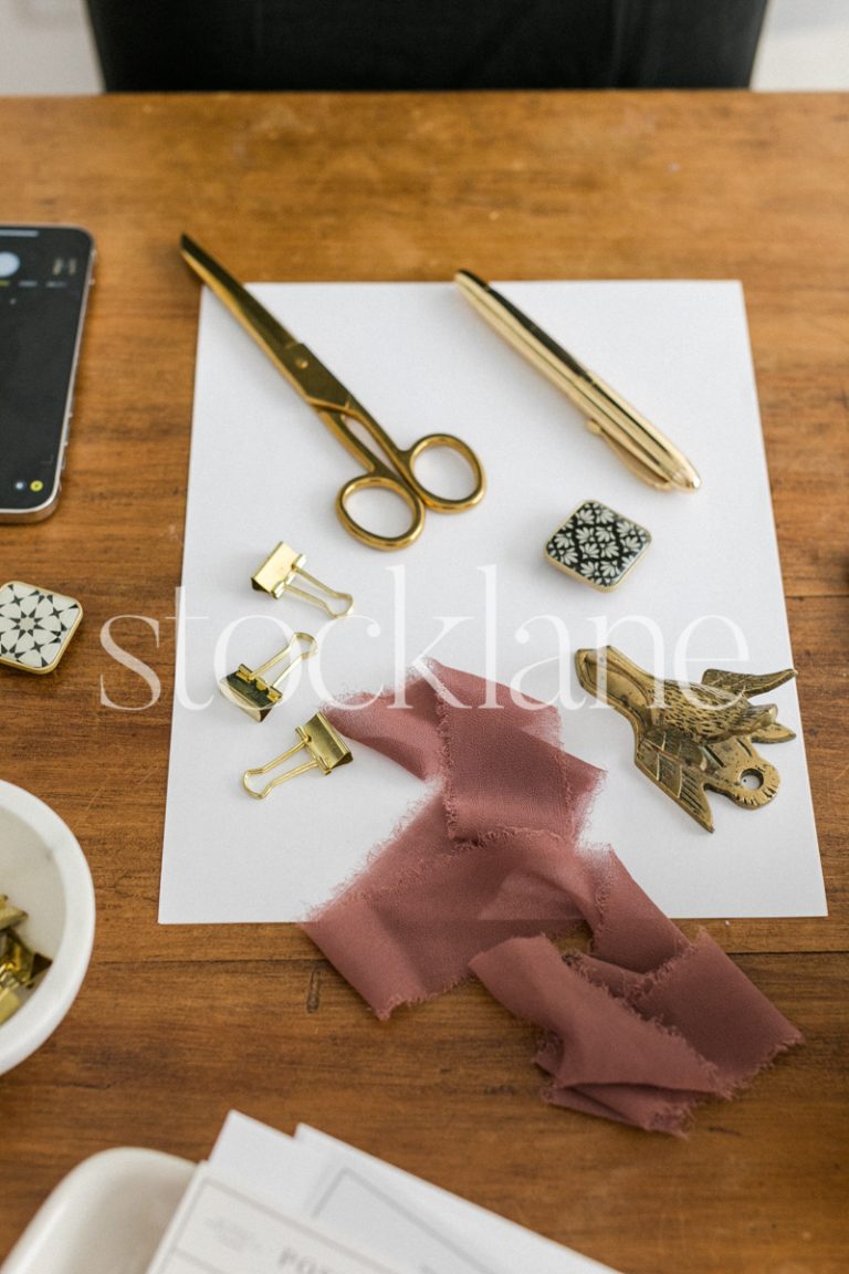 Vertical stock photo of a desk with a flatlay setup in gold and dark pink.