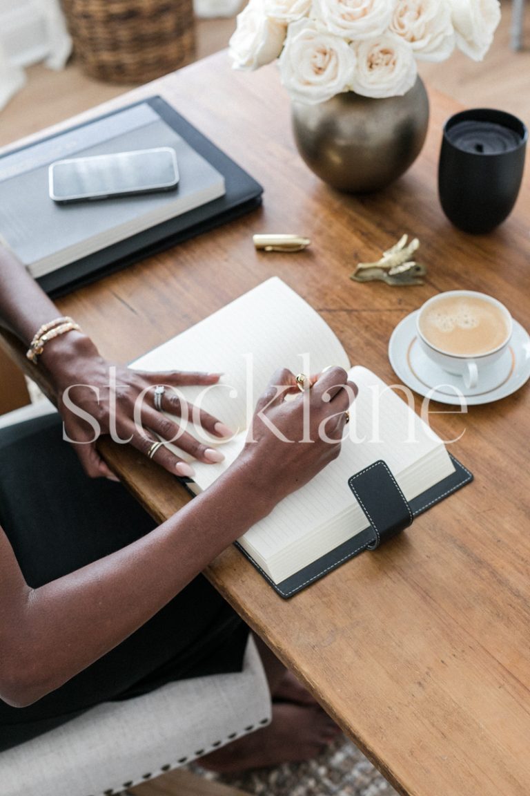 Vertical stock photo of a woman sitting an her desk, writing on her journal.