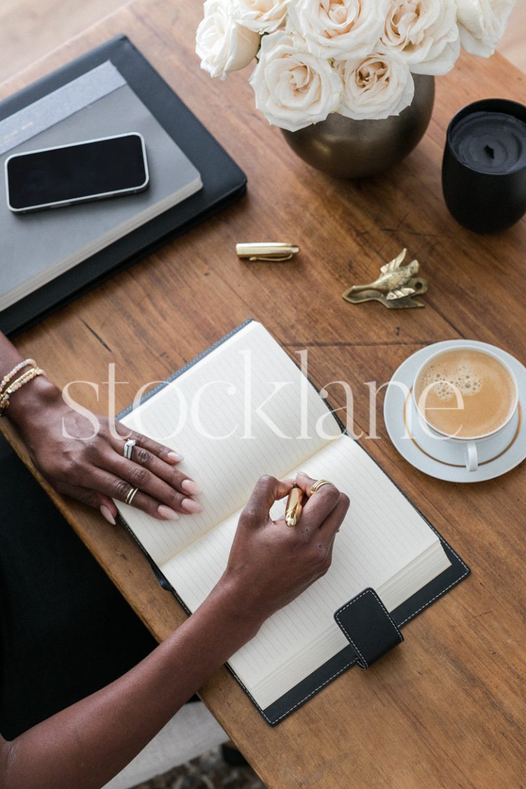 Vertical stock photo of a woman sitting an her desk, writing on her journal.