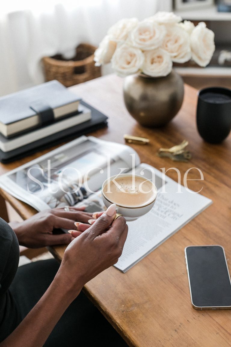 Vertical stock photo of a woman sitting at her desk, having a coffee and reading a magazine.