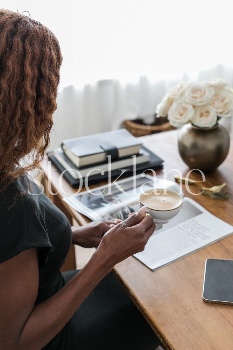 Vertical stock photo of a woman sitting at her desk, having a coffee and reading a magazine.