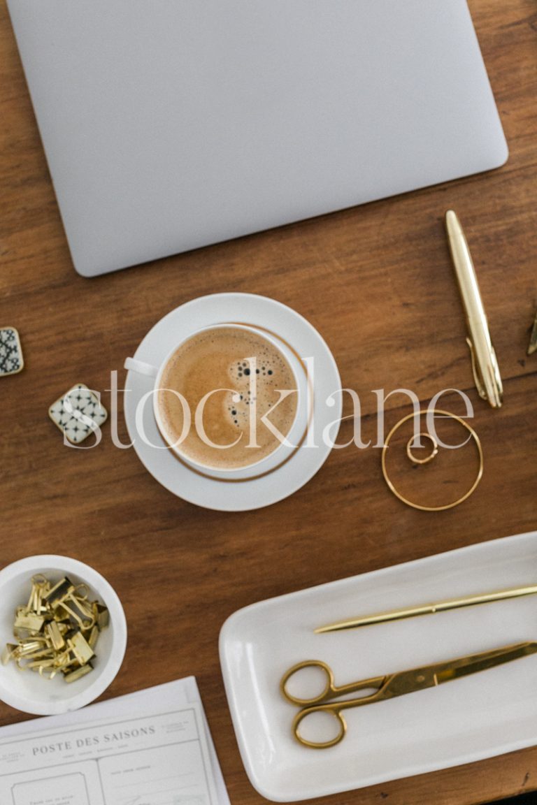 Vertical stock photo of a desk with a computer, a cup of coffee and other desk supplies, in gold and neutral colors.