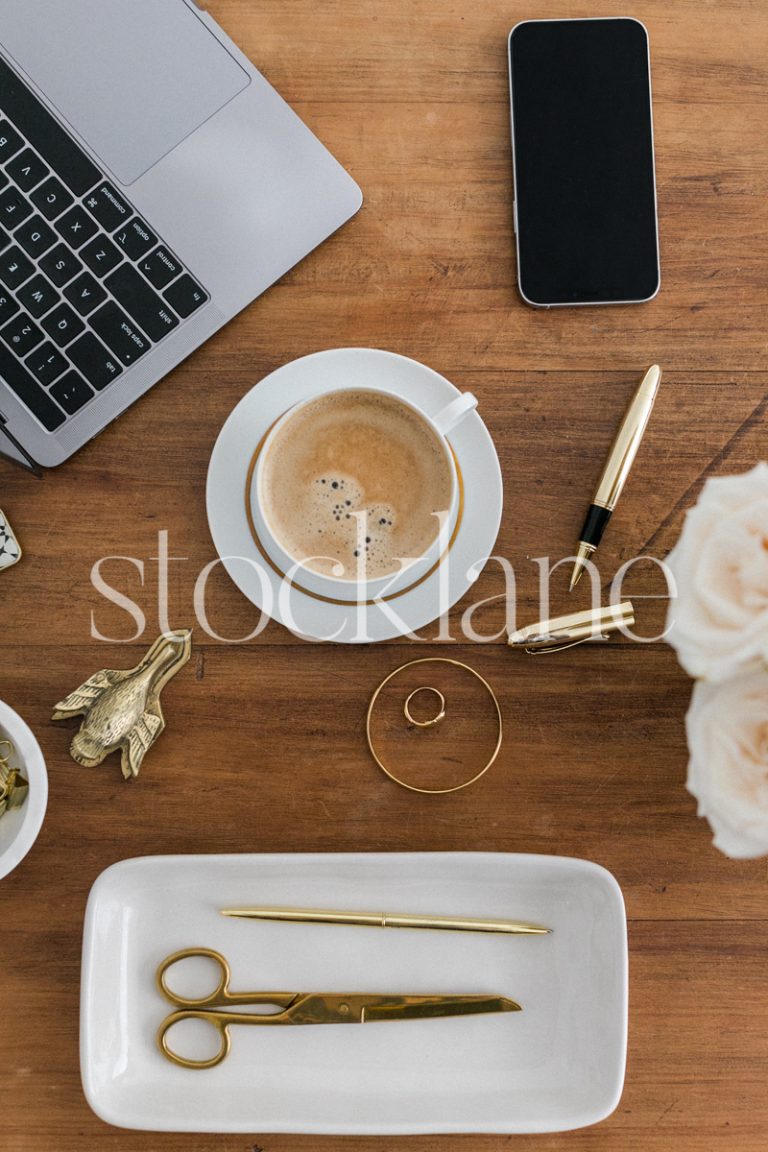 Vertical stock photo of a desk with a computer, a cup of coffee and other desk supplies, in gold and neutral colors.