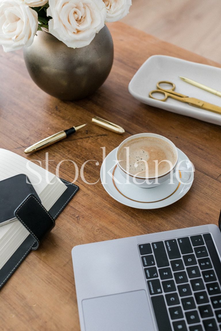 Vertical stock photo of a desk with a computer, a cup of coffee and other desk supplies, in gold and neutral colors.