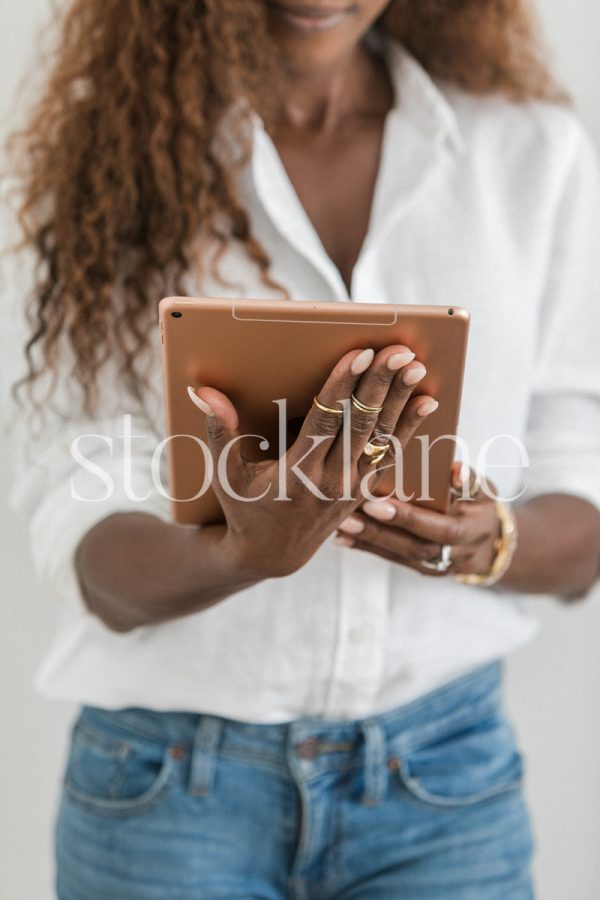 Vertical stock photo of a woman wearing a white shirt and jeans, holding an iPad.