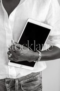 Vertical black and white stock photo of a woman wearing a white shirt and jeans, holding an iPad.