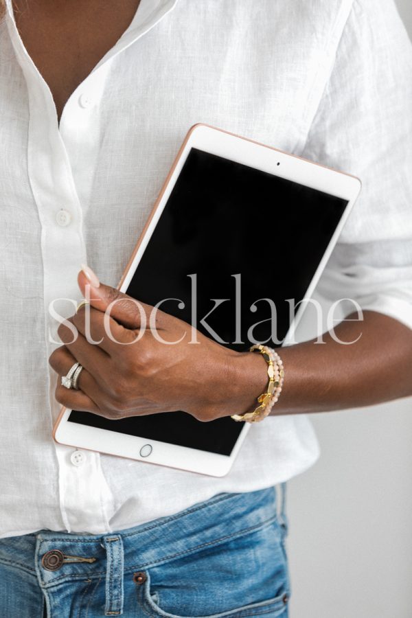 Vertical stock photo of a woman wearing a white shirt and jeans, holding an iPad.