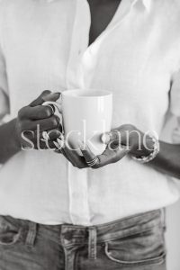 Vertical black and white stock photo of a woman wearing a white shirt and jeans, holding a cup.