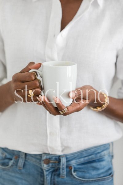 Vertical stock photo of a woman wearing a white shirt and jeans, holding a cup.