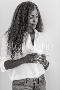Vertical black and white stock photo of a woman wearing a white shirt and jeans, holding a cup.