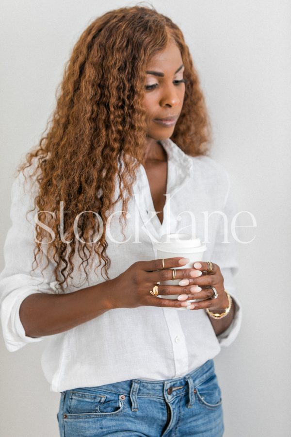 Vertical stock photo of a woman wearing a white shirt and jeans, holding a cup.