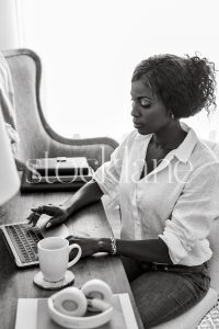 Vertical black and white stock photo of a woman sitting at her desk working on her laptop computer.