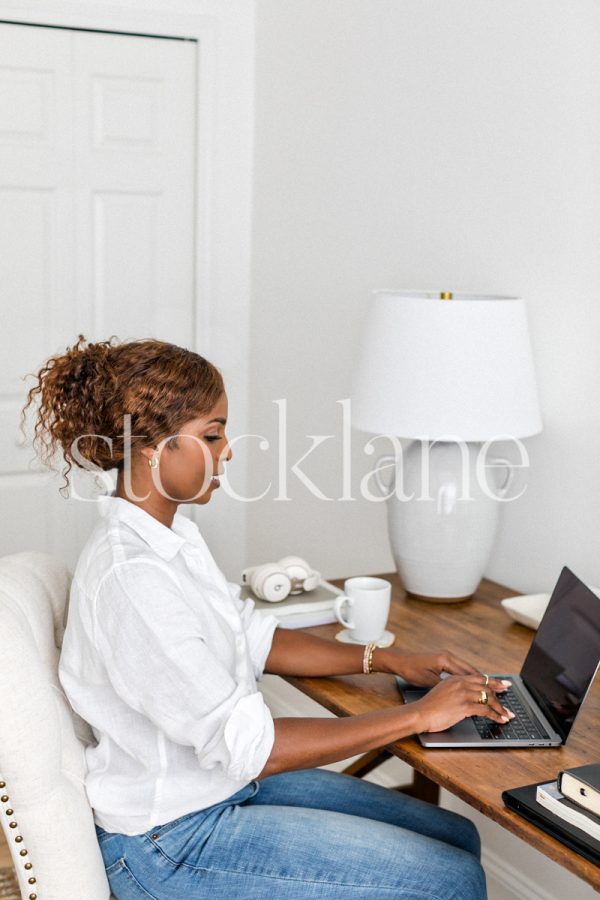 Vertical stock photo of a woman sitting at her desk working on her laptop computer.