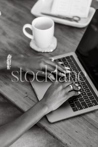 Vertical black and white stock photo of a woman sitting at her desk working on her laptop computer.