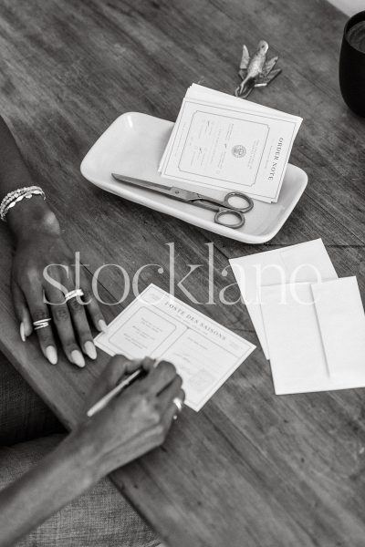 Vertical black and white stock photo of a woman sitting at her desk writing a note.