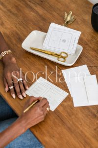 Vertical stock photo of a woman sitting at her desk writing a note.