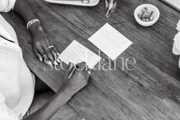 Horizontal black and white stock photo of a woman sitting at her desk writing a note.